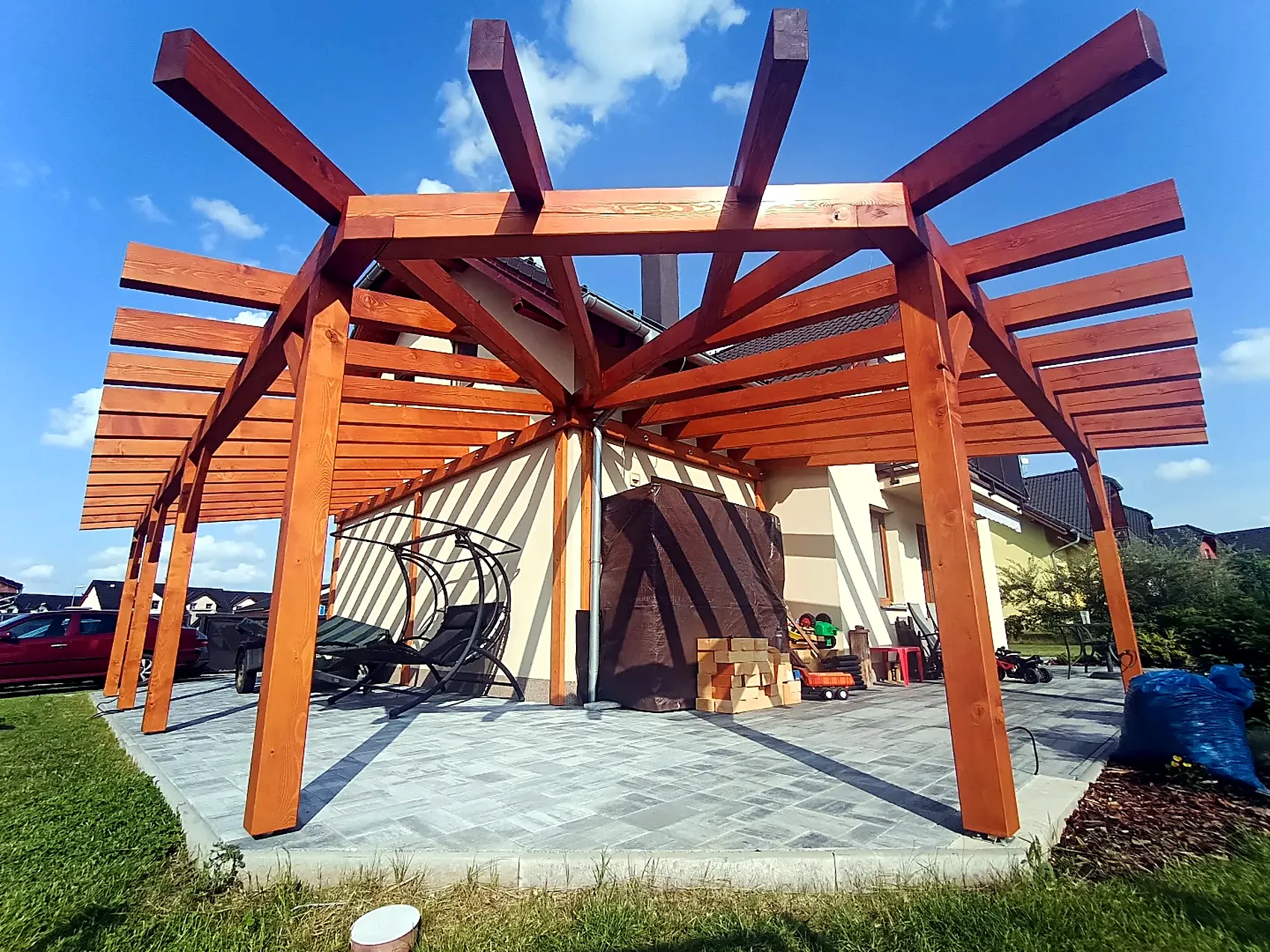 Mohutná pergola ze smrkových KVH hranolů s paprskovitě rozloženými krokvemi nad dlážděnou terasou