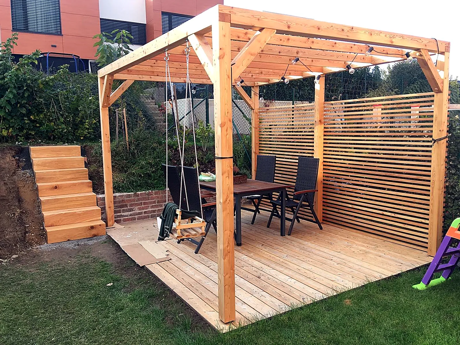 Modřínová pergola s dřevěnou podlahou, houpačkou a stínicí stěnou na zahradě